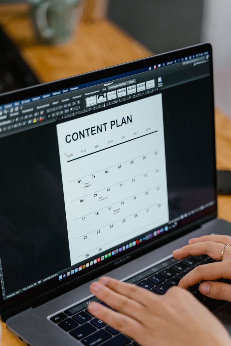 Hands editing a monthly content calendar in a word processor on a laptop.