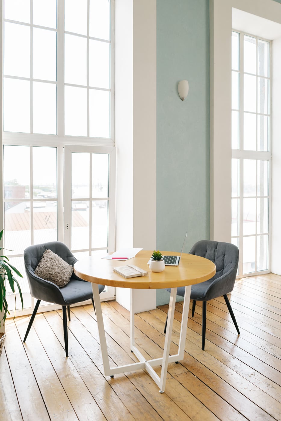 A bright workspace with a laptop on a table beside large windows.